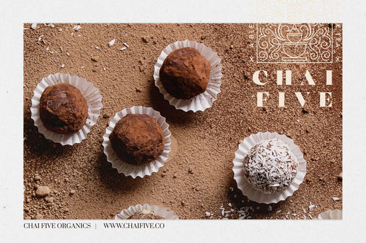 Chocolate truffles in white paper cups on a counter dusted with chocolate powder.